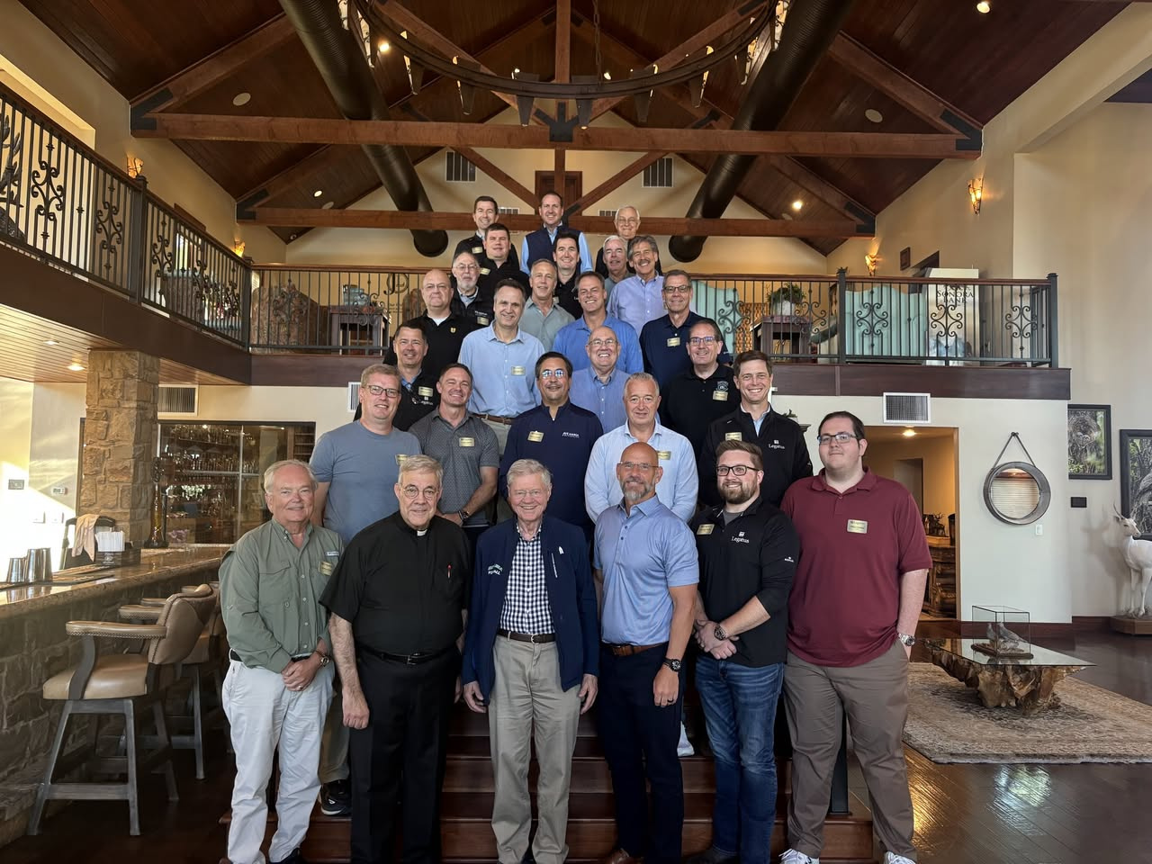 A large group of men stand on the stairs for a group photo in wooden lodge