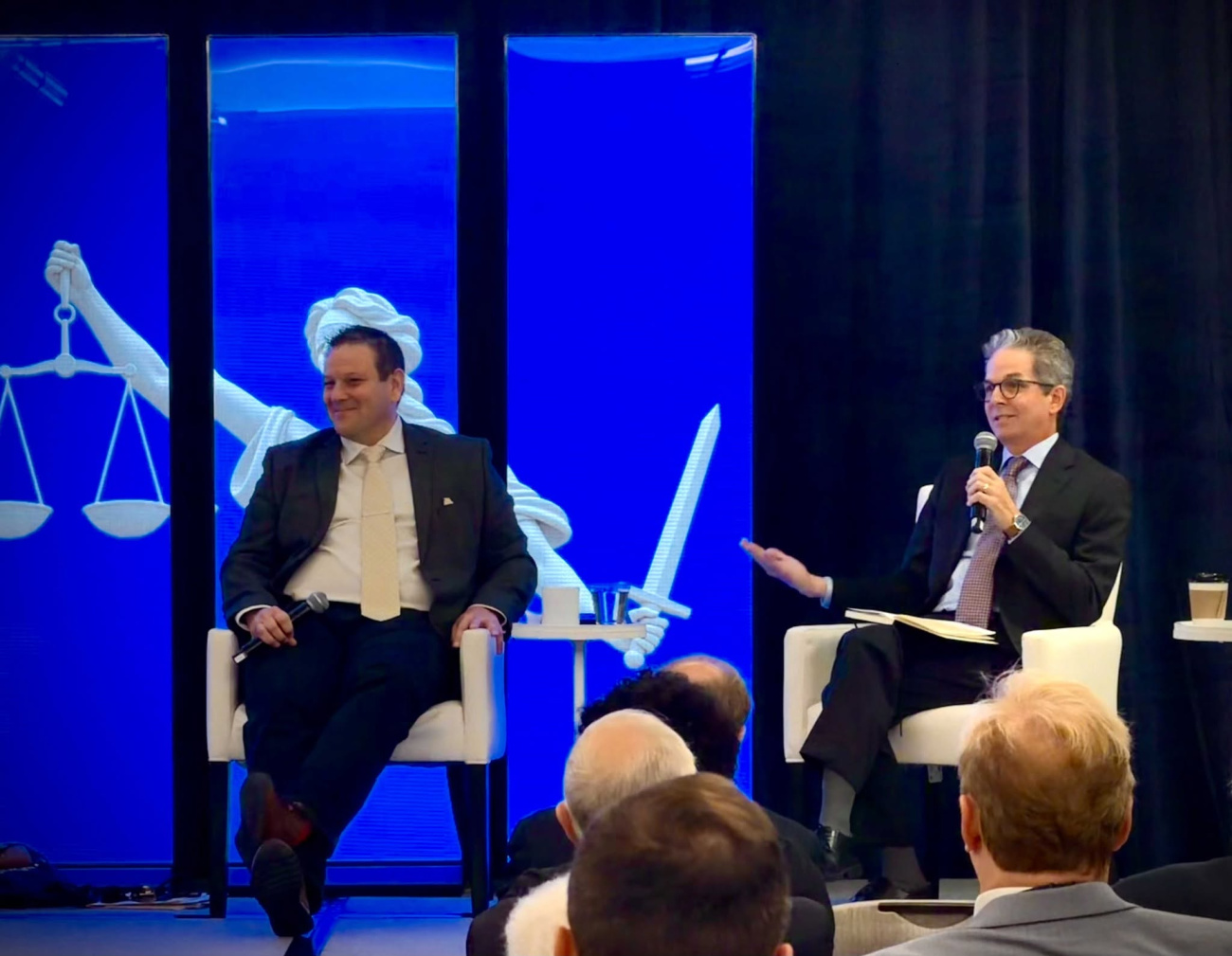John Pinheiro sitting on stage with another panelist, speaking to an audience