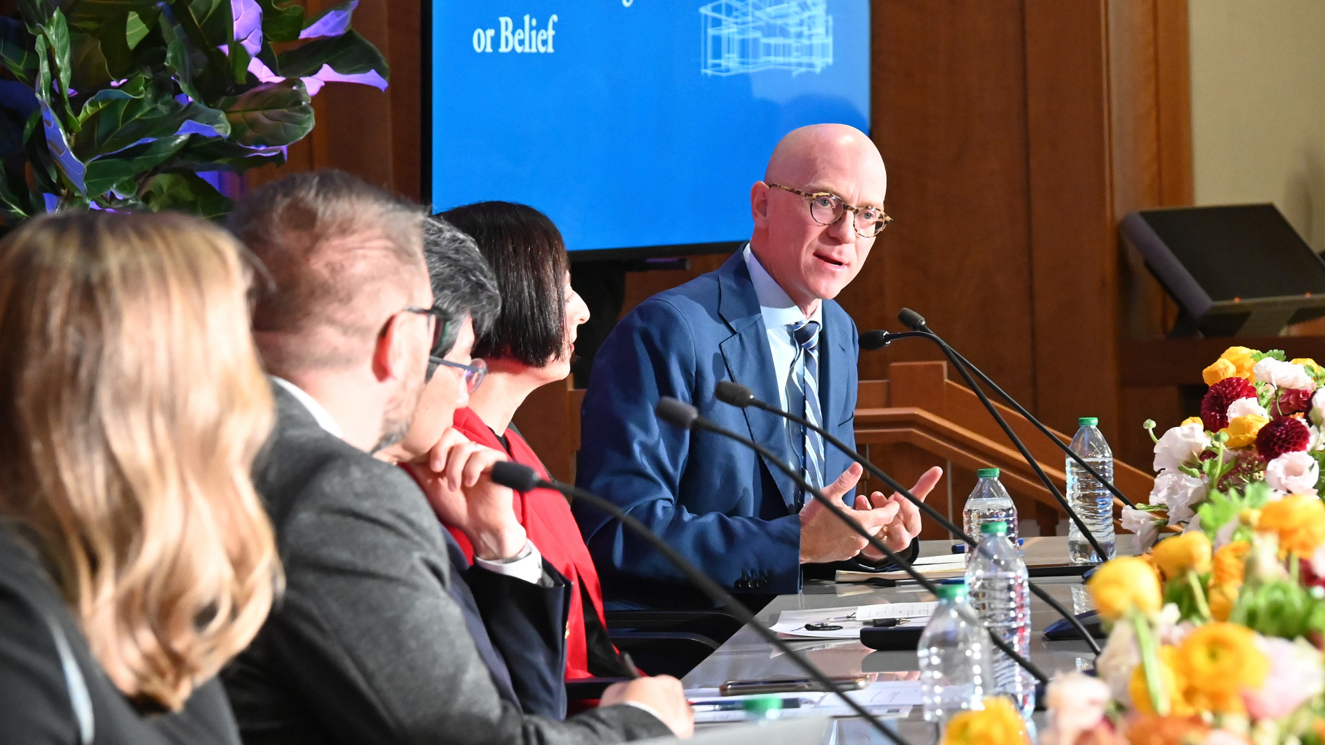 Michael Miller speaks into a microphone at a table of featured panelists on stage