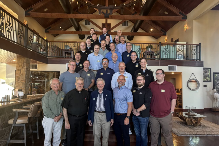 A large group of men stand on the stairs for a group photo in wooden lodge
