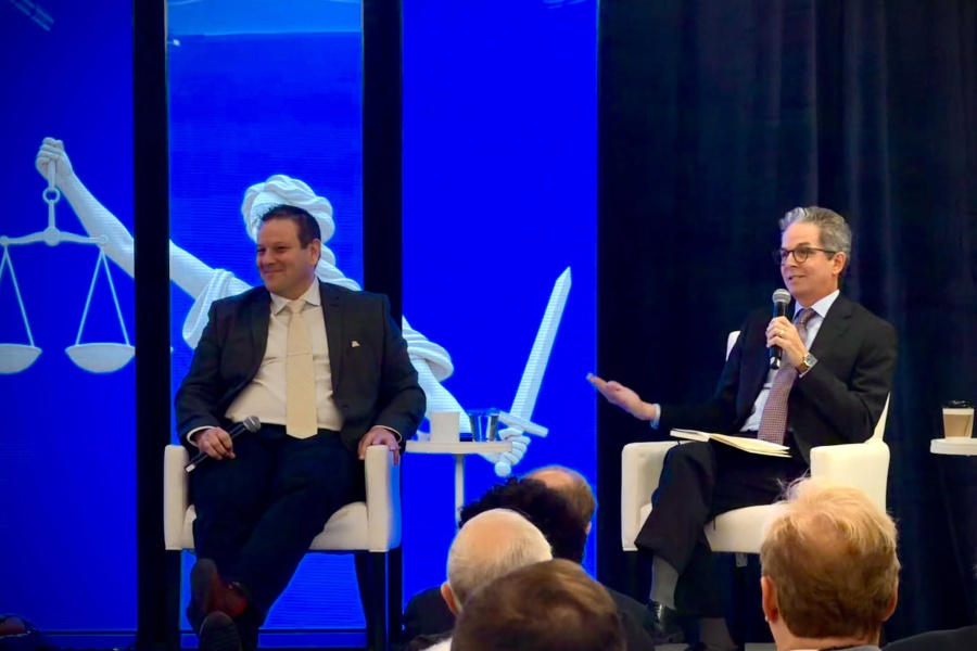 John Pinheiro sitting on stage with another panelist, speaking to an audience