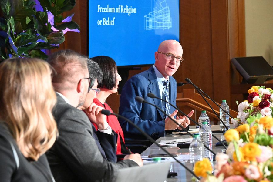 Michael Miller speaks into a microphone at a table of featured panelists on stage